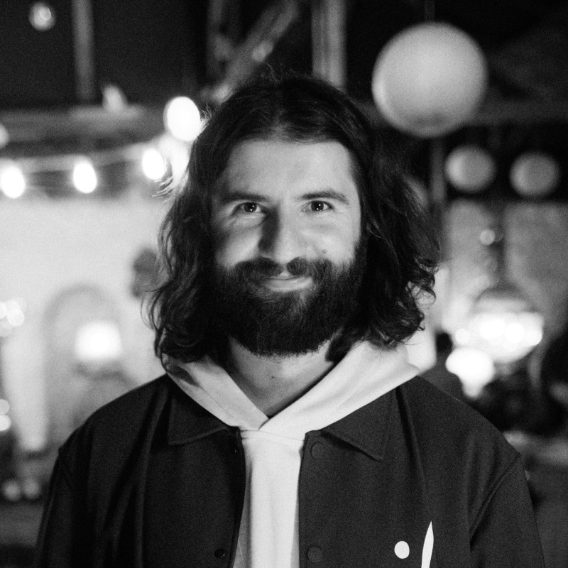 Portrait of a man with brown hair and glasses on a flat gray background.