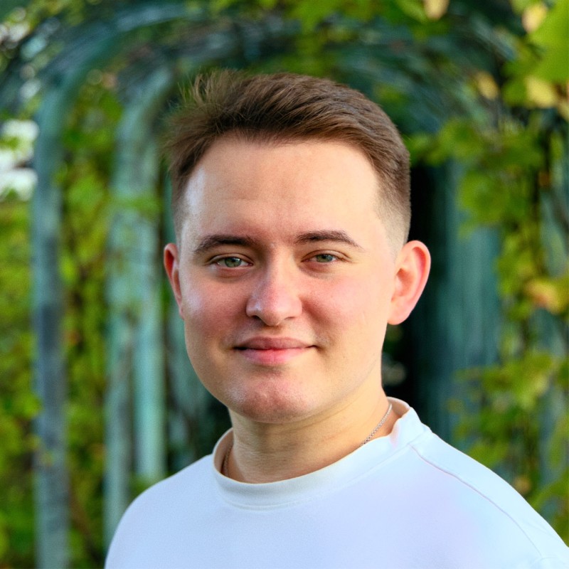 Portrait of a man with brown hair and glasses on a flat gray background.